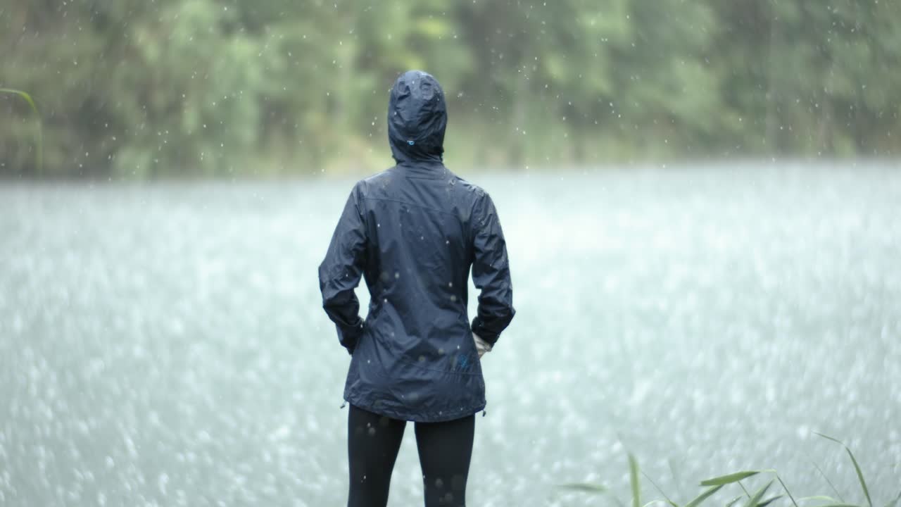 Woman stands in the pouring rain against the background of a lake. Shot on super slow motion camera 1000 fps.