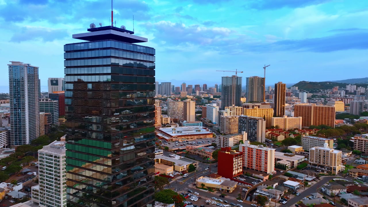 Voando para mais perto do edifício alto com fachada espelhada na paisagem de Honolulu, Havaí, EUA. Imagens de drone sobre a cidade ao pôr do sol