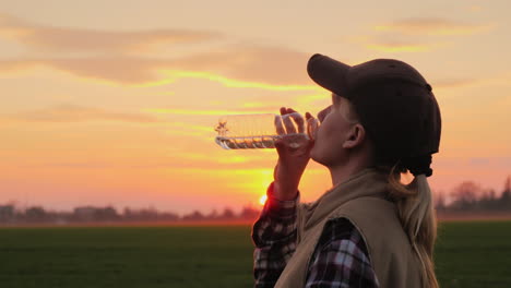 Müde-Bäuerin,-Die-Bei-Sonnenuntergang-Sauberes-Wasser-Aus-Der-Flasche-Trinkt