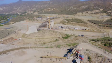 drone sobrevuela la vista del sitio incompleto de construcción del muro de la presa monte grande y maquinaria para obras de tierra, república dominicana - adelante