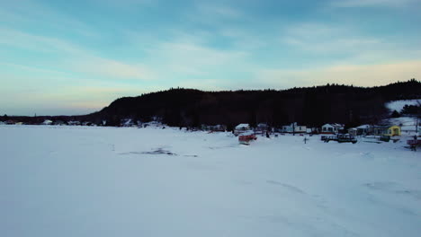 Fliegende-Drohne-über-Häusern-Und-Einem-Zugefrorenen-See-Im-Winter-In-Kanada