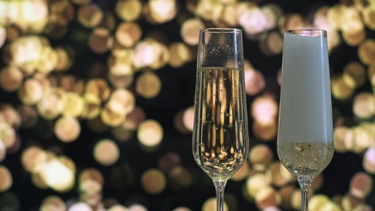 Due flûte di champagne, uno riempito con vino spumante, su uno sfondo di luci bokeh dorate. La scena emana celebrazione ed eleganza, perfetta per occasioni festive o Capodanno