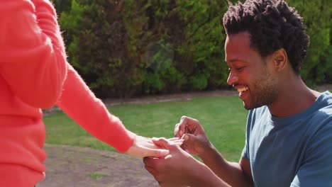 happy biracial man on knees putting engagement ring on woman hand