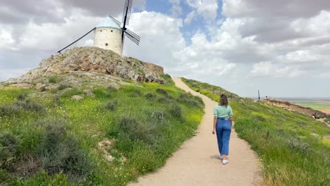 joven rubia campesina caminando hacia un viejo molino de viento en un prado en un día soleado