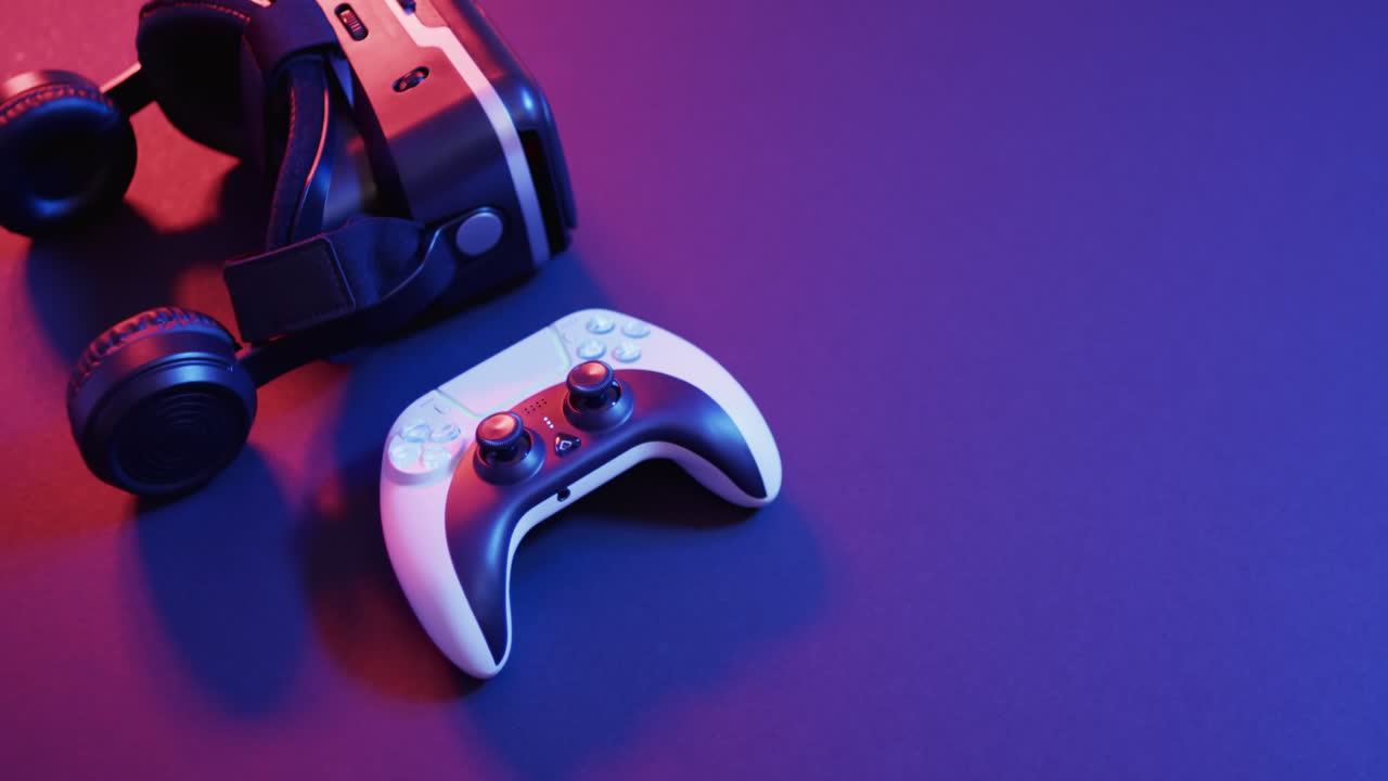 Video of close up of video game pad controller and vr headset with copy space on neon background
