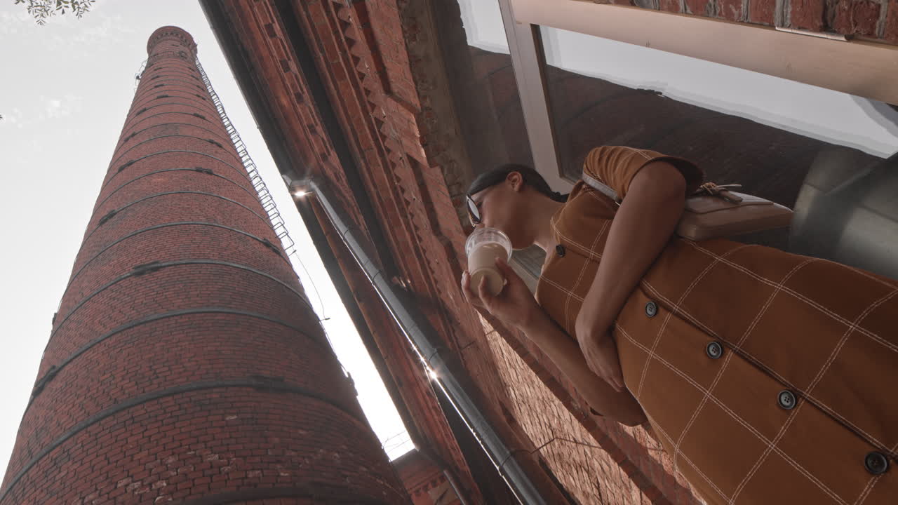 Woman Drinking Iced Coffee by Brick Tower