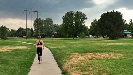 slow motion running woman runs during stormy skies along a park pathway. sleek and fit she inspires others to get out and run despite challenges including weather