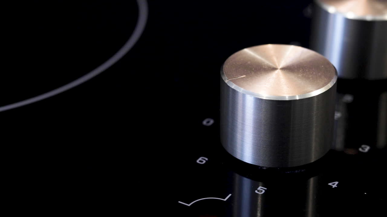 un primer plano de una mano girando la perilla de una estufa eléctrica o vitrocerámica