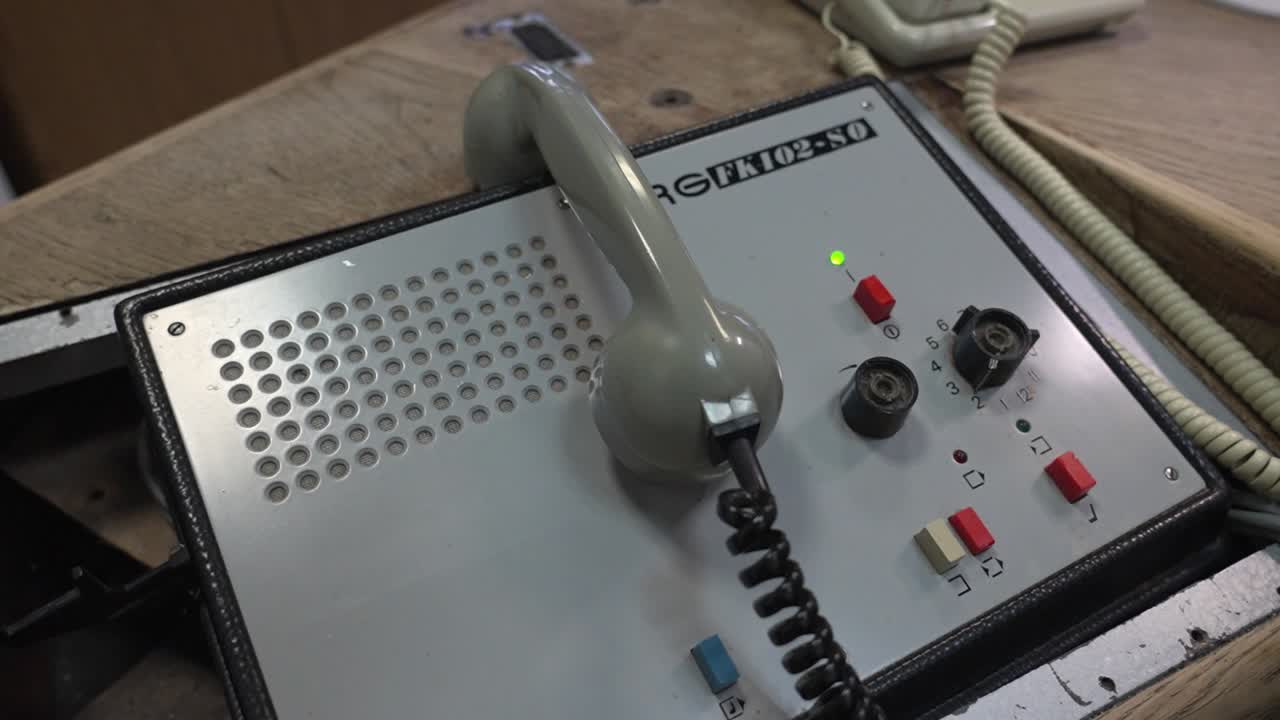 An old railway telephone system with a grey handset, buttons, and control dials in a station office