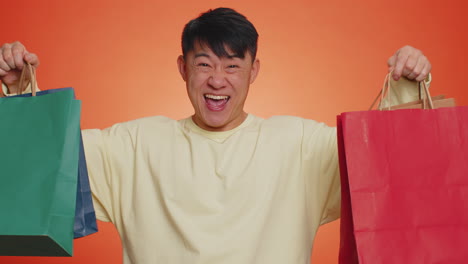 asian man showing shopping bags, advertising discounts, smiling looking amazed with low prices