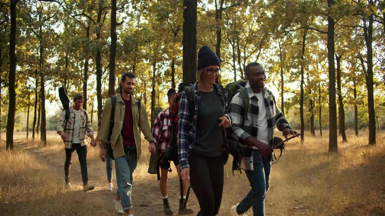 Happy people in hiking clothes and with backpacks walk in pairs, one after another, through the summer forest. Happy group of people While hiking in summer