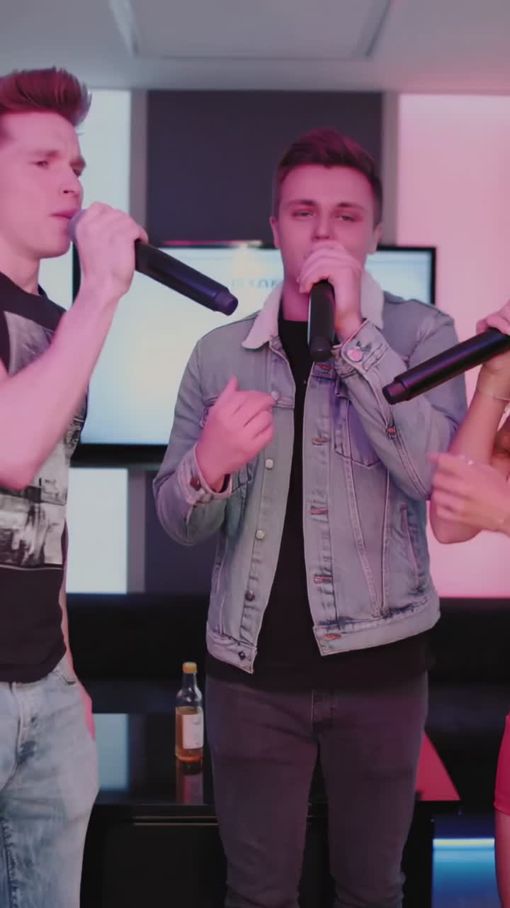 Vertical video: Beat dropping spurring friends singing with mics to lyrics screen in karaoke lounge