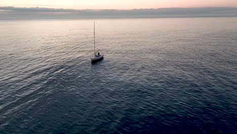 Una-Toma-Aérea-Al-Atardecer-De-Las-Aguas-Del-Mar-Que-Revela-Un-Barco-Con-Una-Vela-Baja