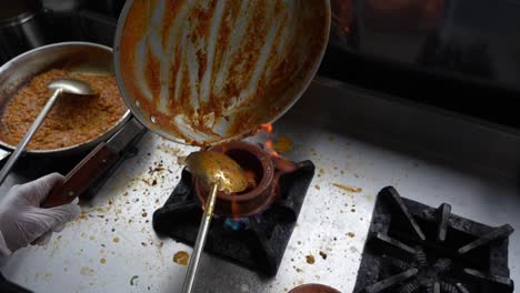 chef transfers curry from a pan into a heated clay pot on a stove at a commercial kitchen