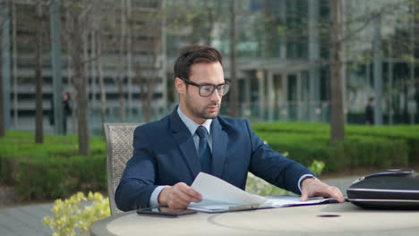 Young-adult-businessman-organizing-documents-or-paper-materials-in-clipboard-sitting-working-in-open-air-at-green-park