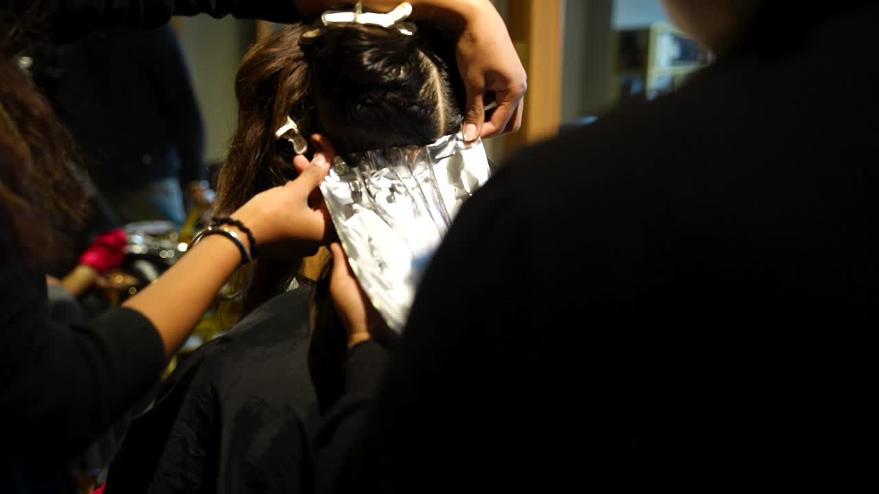 Stylist applies foil to sectioned hair during a color treatment in a salon setting