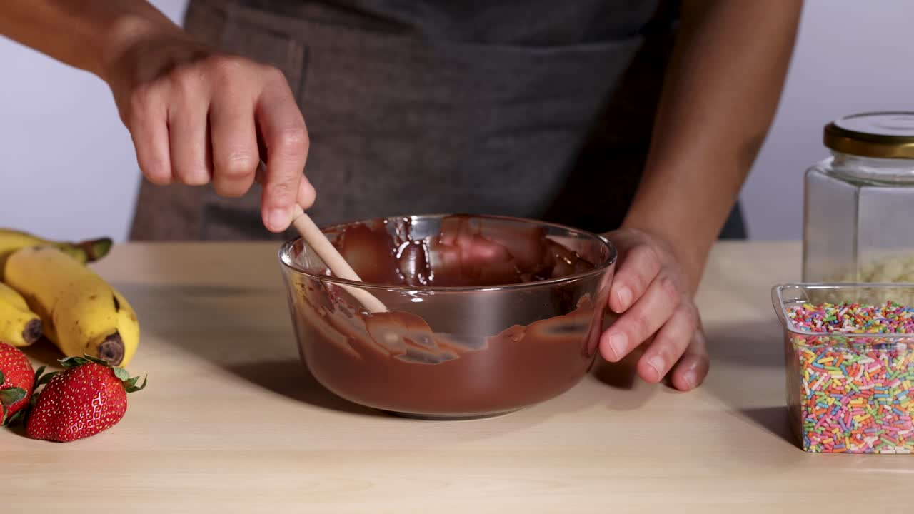 manos sumergiendo plátanos y fresas en chocolate derretido con salpicaduras