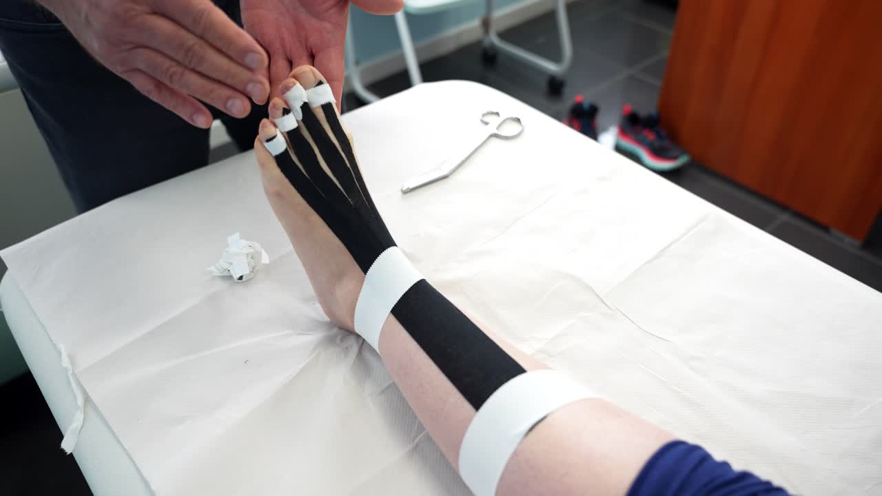 el fisioterapeuta pone cinta de kinesiología en la pierna y los dedos de los pies de la mujer