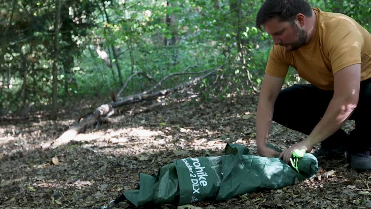 숲 지역에 있는 동안 텐트 천을 굴리는 남자, 보기 확대