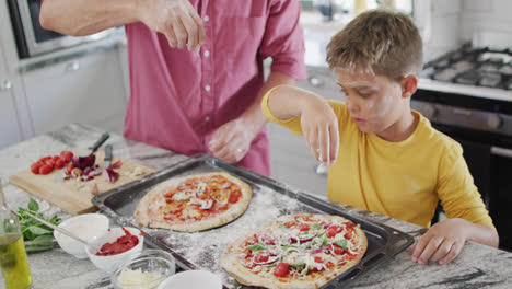 Happy-caucasian-grandfather-and-grandson-making-pizza-in-kitchen,-slow-motion