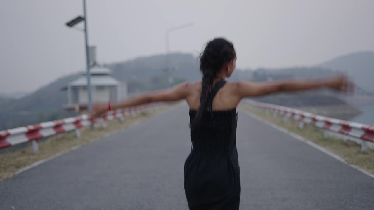 A young woman walks and expresses joy on a road near a dam and lake