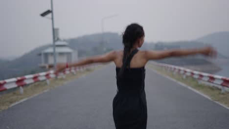 a young woman walks and expresses joy on a road near a dam and lake