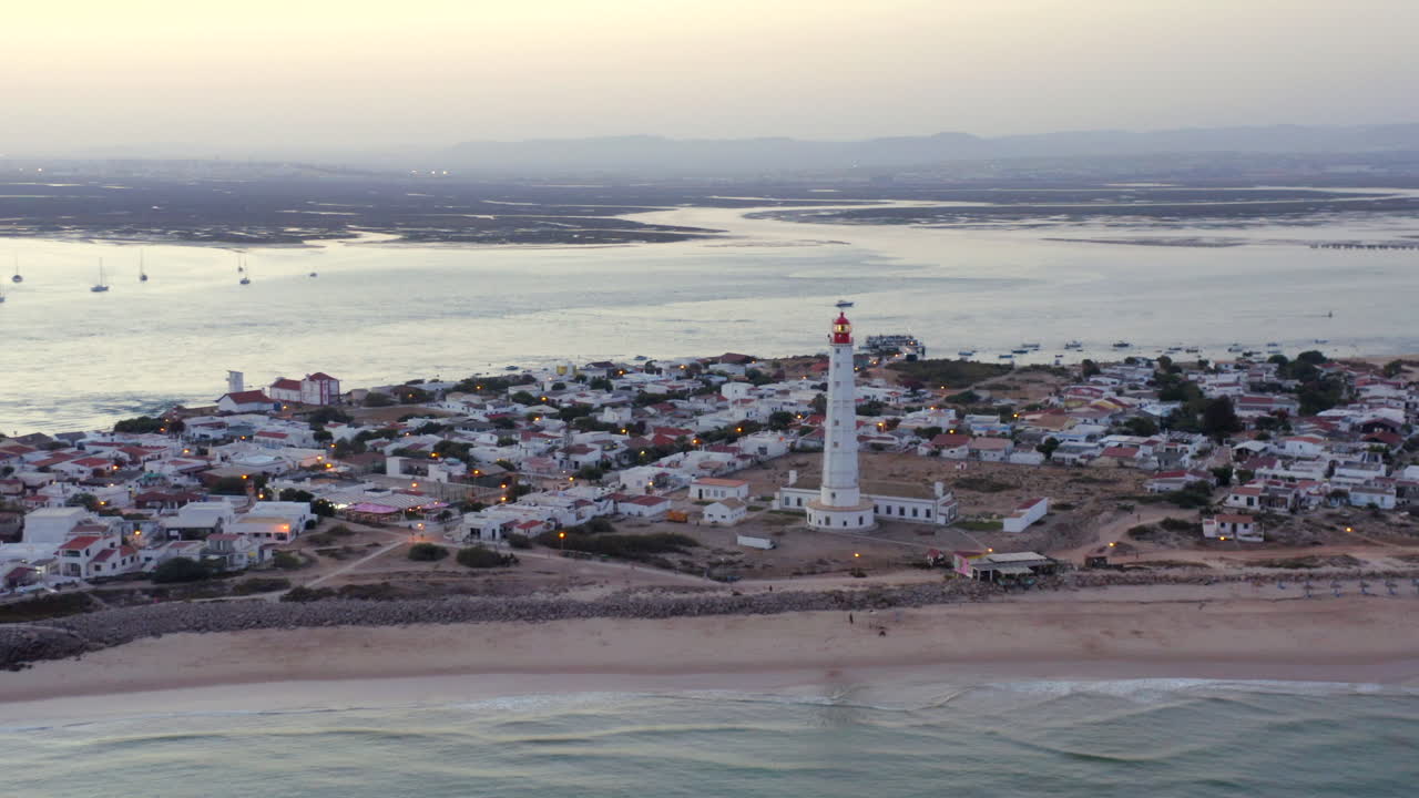 Torre bianca del faro e case in città all'alba, luce del tramonto, vista aerea