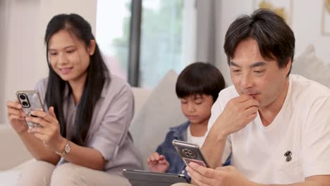 a family of three enjoys a moment together on a sofa, engaging with smartphones in a bright, relaxed living room