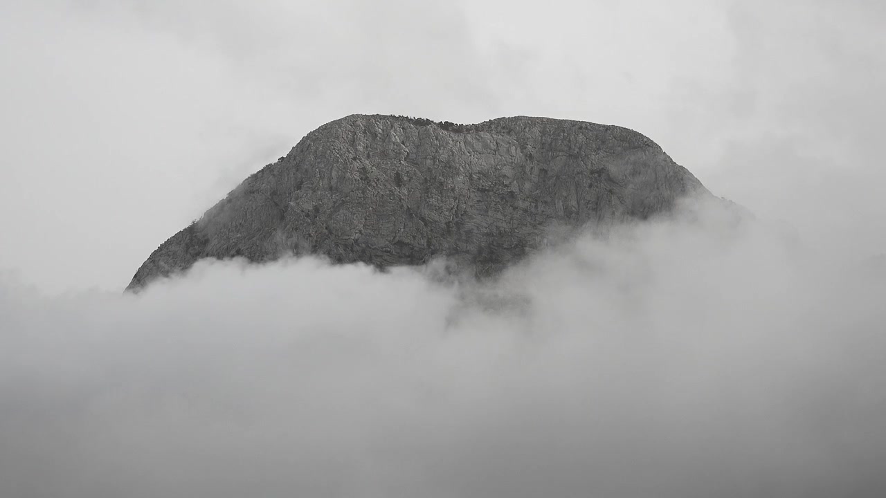 Cima rocciosa di montagna circondata da dense nuvole in movimento