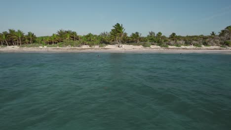 Aerial-view-distancing-from-Xpuha-Beach-in-Riviera-Maya,-Mexico,-with-waves-gently-caressing-the-shoreline