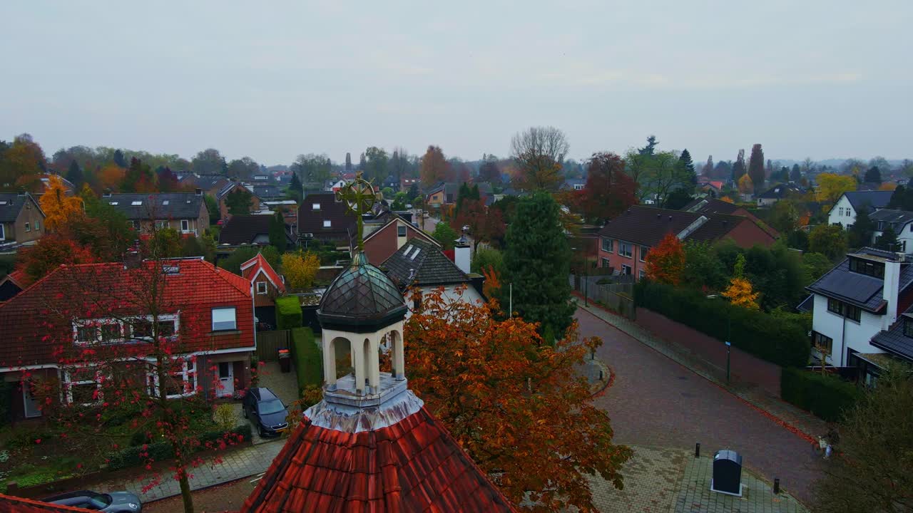 A beautiful old crucifix overlooks a small suburban neighborhood in the Netherlands on an overcast autumn day. A cyclist bicycles over the nearby road