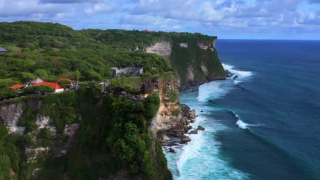 hindu temple of uluwatu on the cliffside overviewing the blue ocean on a cloudy day in bali, indonesia