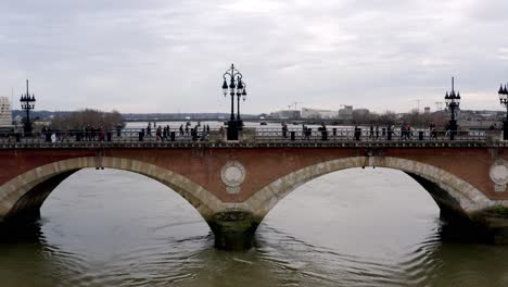 Pont-de-Pierre-Napoleonic-bridge-in-Bordeaux-France-with-people-crossing-the-Garonne-river,-Aerial-dolly-right-tracking-shot