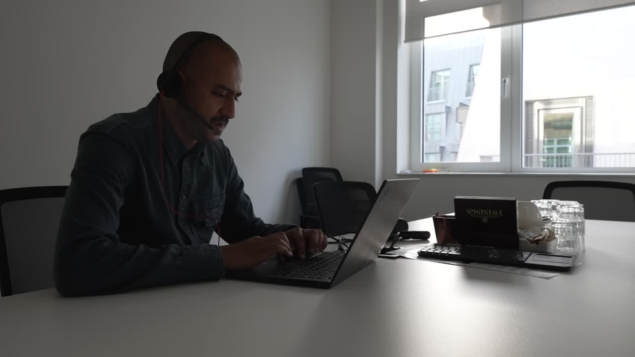 Bald Male Freelancer Wearing Headset Talking Through Laptop In Meeting Room