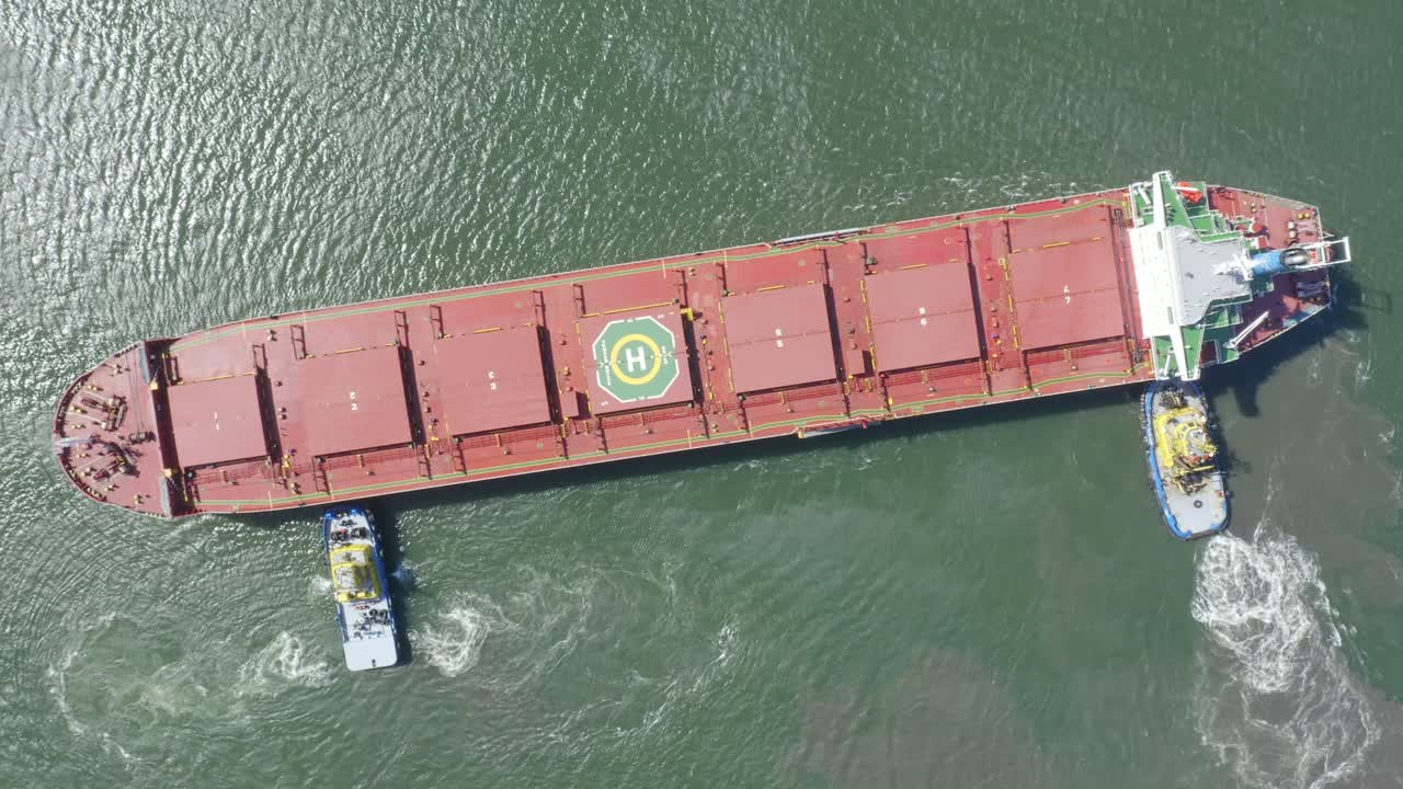 Bulk carrier Navios Sphera arriving to port with assistance of tug boats. Top down aerial view