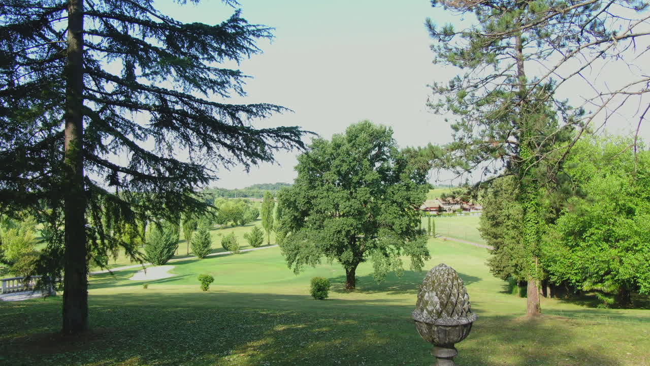 Drohnenaufnahme, die durch hohe Bäume in einem schönen Garten über einer alten Mauer in Italien fliegt