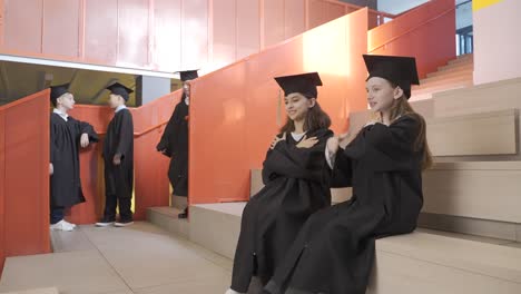 estudiantes de kindergarten felices con toga y birrete jugando y hablando juntos antes de la ceremonia de graduación de preescolar
