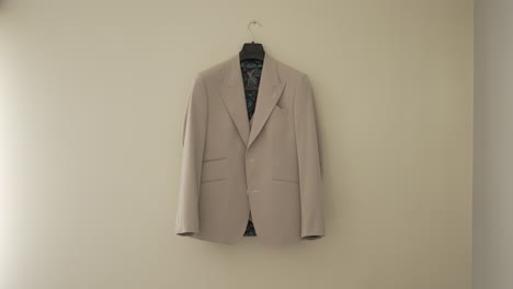 beige suit jacket hanging on a wall, neatly displayed on a black hanger