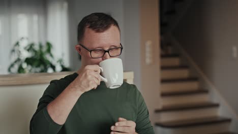 Nachdenklicher-Kaukasischer-Mann-Mit-Down-Syndrom,-Der-Kaffee-In-Der-Heimischen-Küche-Trinkt.