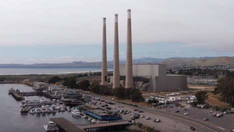 low rising aerial shot of the three famous smokestacks towering above the defunct morro bay power plant in morro bay, california