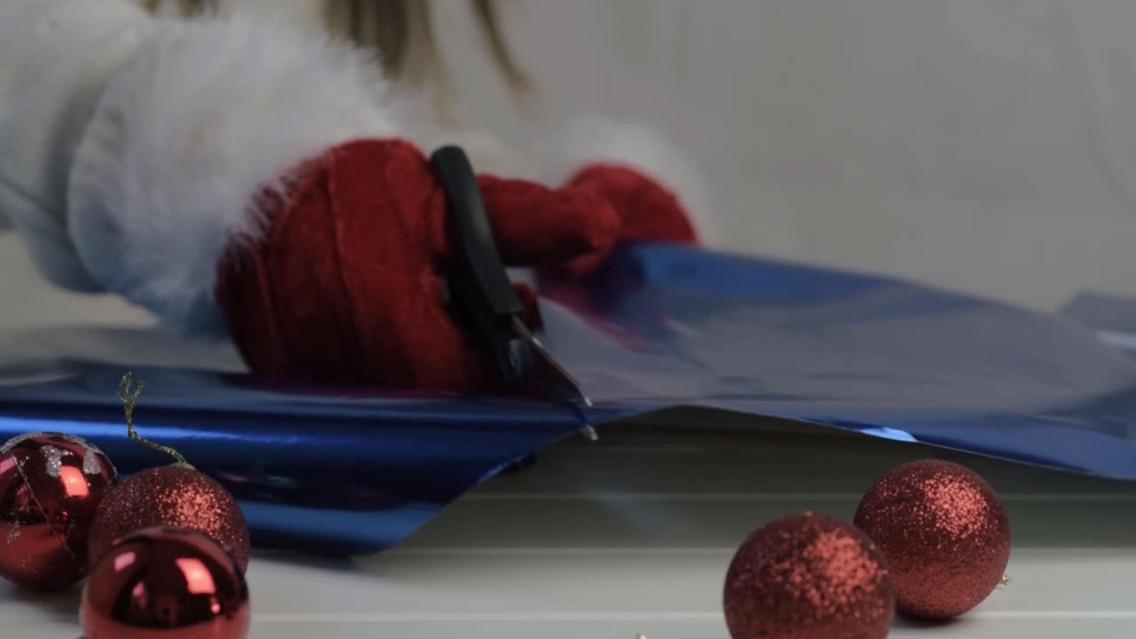 Hand wearing Santa gloves cutting blue Christmas gift paper