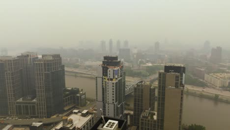 Aerial-view-rising-behind-a-condo,-revealing-Harlem-cityscape-covered-in-thick-forest-fire-smoke,-in-NY,-USA