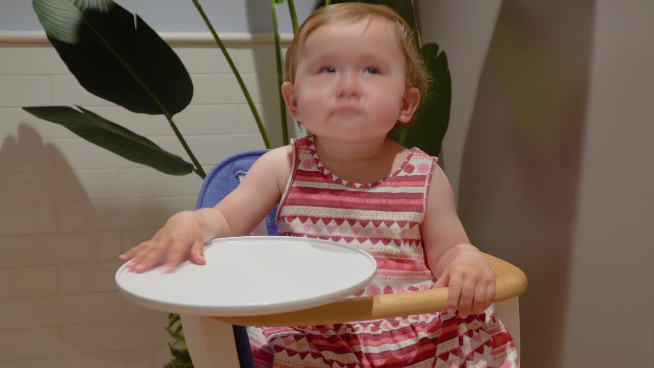 아기 의자에 앉아 간식을 먹고, 손뼉을 치고 테이블에 손을 치는 행복한 아기 소녀