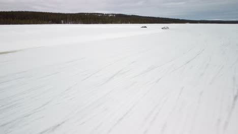 two sport cars drifting on frozen lake in finland during golden hour – aerial winter landscape with a frozen race track low altitude