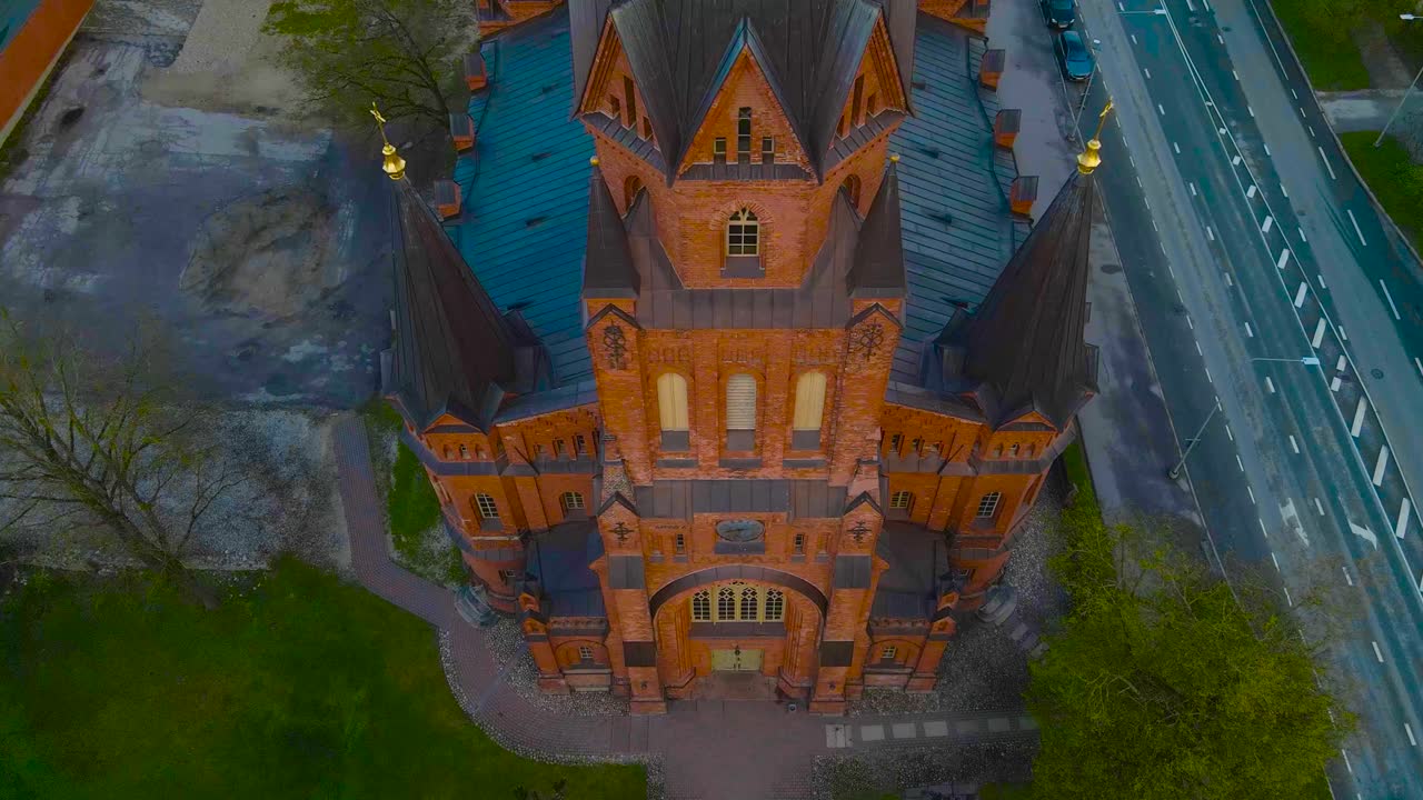 Gorgeous aerial revealing drone footage of a large red brick majestic religous building called Peetri church in Tartu estonia during evening or morning. Church has crosses on towers in urban city area