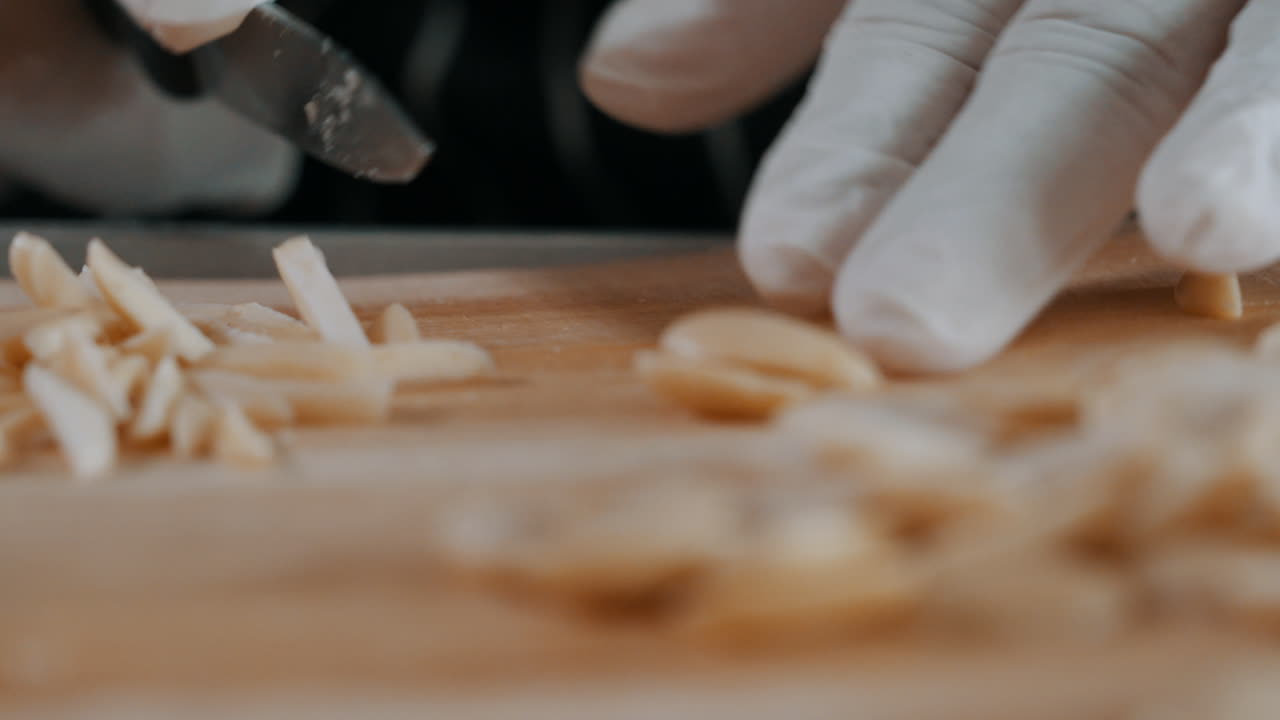 Mano che taglia mandorle a lamelle, produzione artigianale di lamelle di mandorle, primo piano.