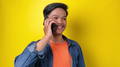 Young-man-in-casual-style-make-a-phone-call-using-mobile-phone,-talking-on-the-phone,-smile-and-greeting-to-friend-on-the-phone,-isolated-on-yellow-background