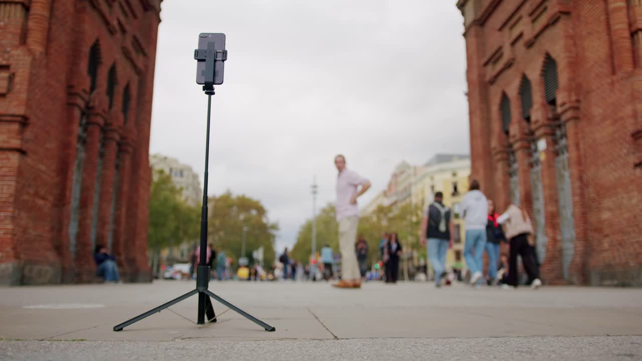Man blogger making videos using selfie stick phone smartphone taking photo with dance for internet blog on street. Young guy tourist having video call on cellphone walking outdoors in Barcelona spain