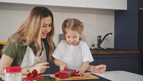 madre feliz mira a la hija pequeña tratando de cortar pimienta