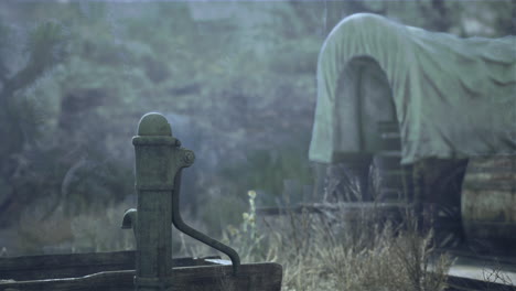 old water pump in the desert with a covered wagon in the background